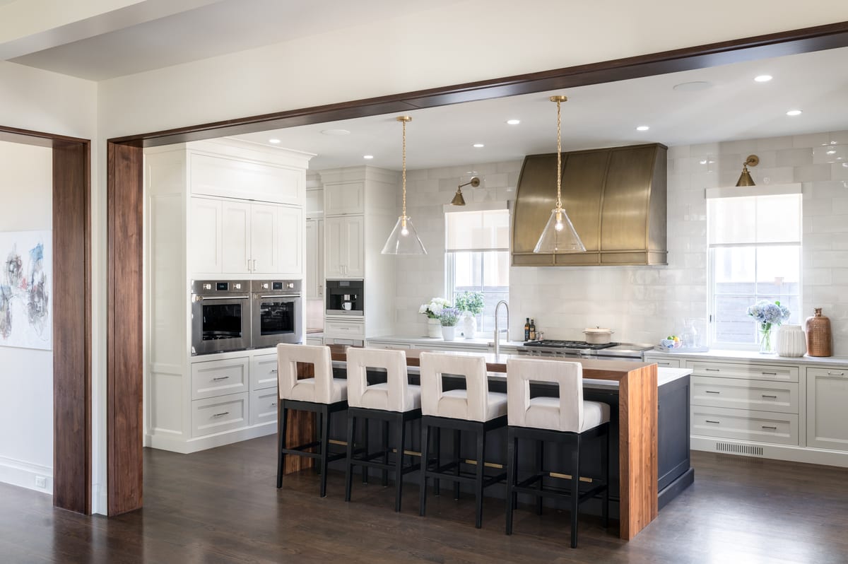 Finished kitchen with island seating, cream bar stools, and a brass range hood